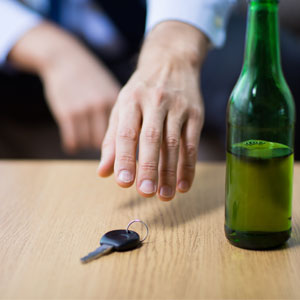 Hand reaching for car keys next to an open beer bottle on a table symbolizing first dwi offense - Law Offices Of Robert Keating, PLLC